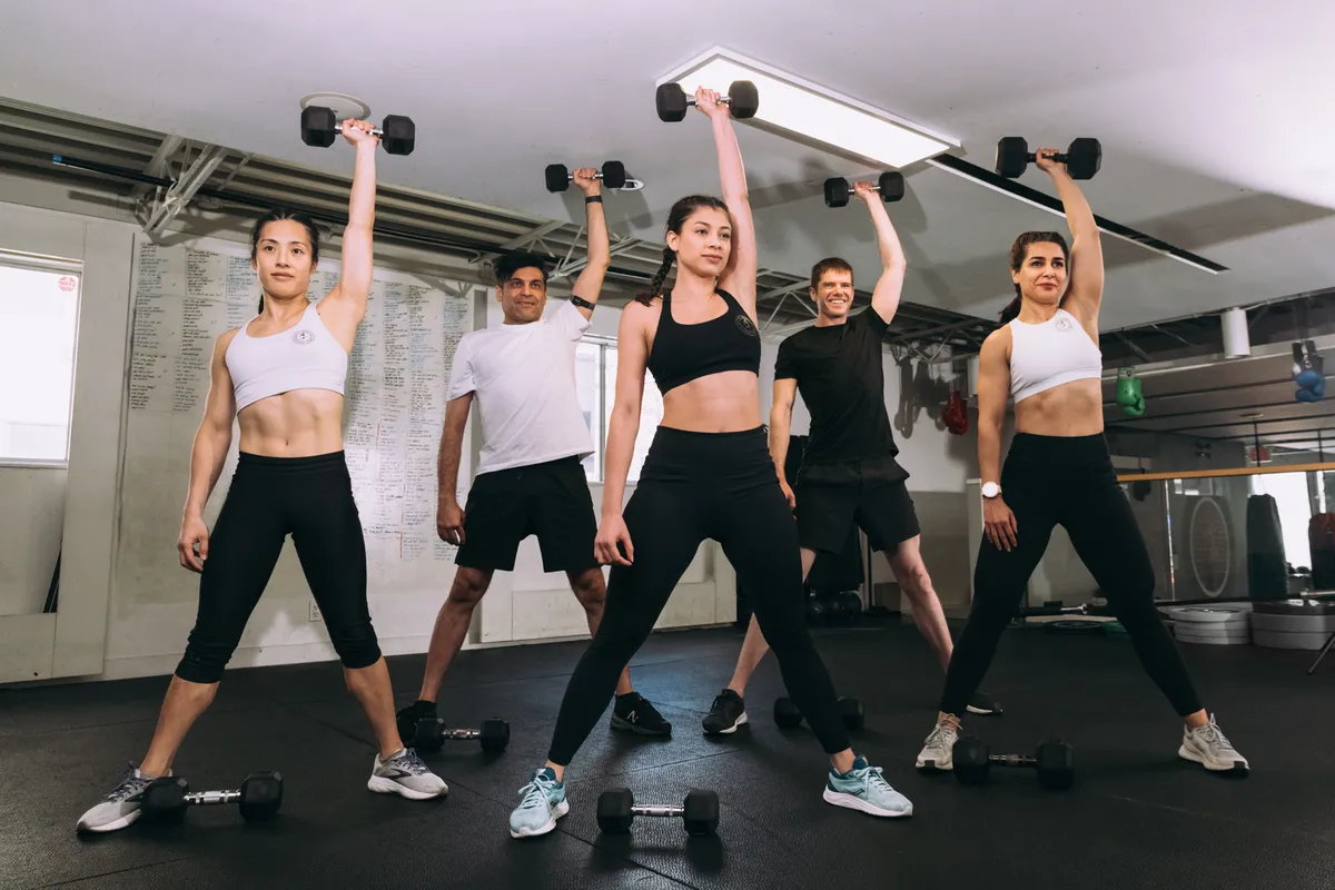 District Warrior members pressing dumbbells overhead in a group conditioning session